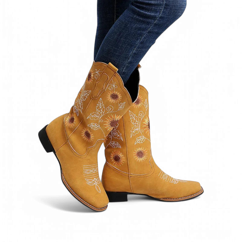 Side view of the yellow embroidered boot worn with skinny jeans, legs crossed.
